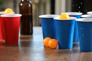 Bira pong oyunu. İçkili plastik bardaklar ve toplar ahşap masada, yakın plan.