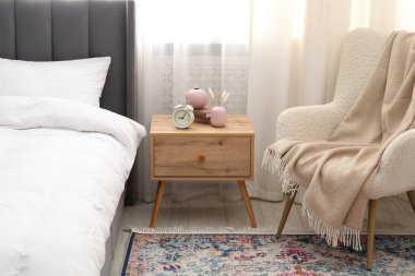 Yatağın yanında alarm saati ve dekorasyonu olan komodinin yanında.