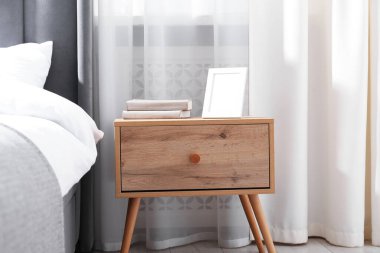 Yatağın yanında kitap ve çerçeve olan komodin.