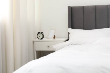 Alarm saati ve yatağın yanındaki çerçeveli komodinin yanında.