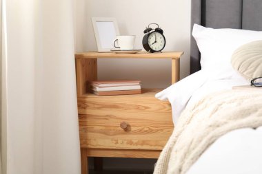 Yatağın yanında çalar saati, kahvesi ve çerçevesi olan bir komodin.