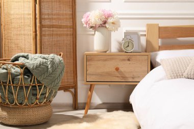 Komodinin yanında çalar saat ve yatağın yanında çiçekler var.