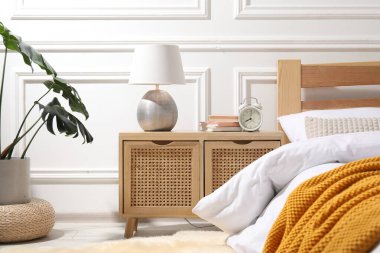 İçinde lamba, çalar saat ve yatağın yanında kitaplar olan komodin.