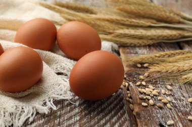 Çiğ yumurta, kumaş ve buğday dalları ahşap masada, yakın plan.