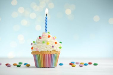 Kekin içinde yanan mum ve masasında mavi arka planda bulanık ışıklarla duran şekerler. Metin için boşluk