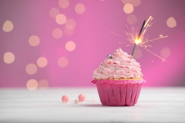 Pembe arka planda, bulanık ışıklarla kek masasında maytap yakmak. Metin için boşluk