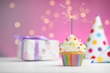 Pembe arka planda bulanık ışıklarla kek ve parti dekorunda yanan maytap. Metin için boşluk