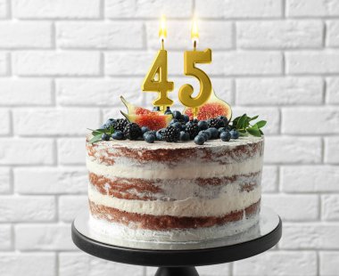 Meyveli lezzetli pasta ve beyaz tuğla duvarın yanında yanan mumlar. 45. Doğum günü veya diğer özel günler