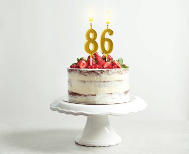 Meyveli lezzetli pasta ve beyaz arka planda yanan mumlar. 86. yaş günü veya diğer özel günler