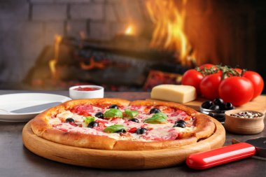 Fırına karşı gri masada taze pişmiş pizza ve malzemeler.