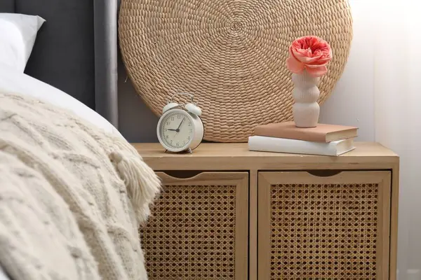 Yatağın yanında çalar saati, dekorasyonu ve kitapları olan bir komodin.