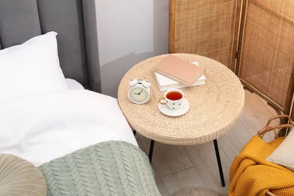 Çalar saati olan yan masa, bir fincan çay ve yatağın yanında kitaplar, manzaranın üstünde.