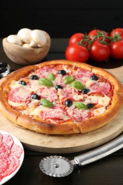 Lezzetli pizza, malzemeler ve siyah ahşap masa, yakın plan.