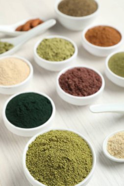 Beyaz ahşap masadaki farklı süper yiyecek tozları, yakın plan.