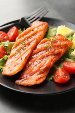 Lezzetli ızgara somon, marul, domates ve limonla servis edilir.