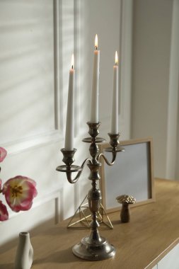 Beyaz duvarın yanında yanan mumlar ve dekorlarla süslü zarif bir şamdan.