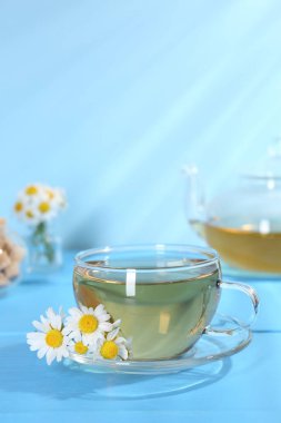 Cam bardakta nefis papatya çayı ve açık mavi ahşap masada taze çiçekler, yakın plan.