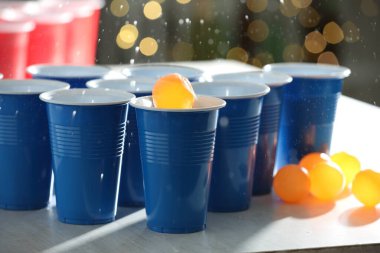 Turuncu top, açık ahşap masada plastik bardağa düşerken bulanık ışıklara karşı, yakın plan. Bira pong oyunu