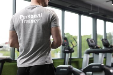 Spor salonunda yazılı tişört giyen kişisel antrenör, yakın plan. Arka plan