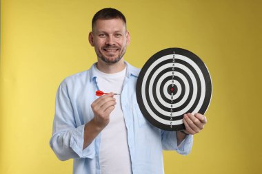 Hedef alınıyor. Sarı arka planda ok ve dart tahtası olan adam.