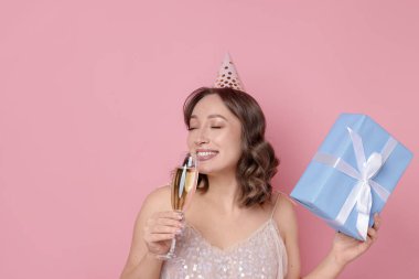 Doğum günü kutlaması. Bir bardak köpüklü şarap ve pembe arka planda bir hediye.