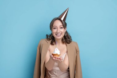 Doğum günü kutlaması. Açık mavi arka planda kek yiyen kadın.