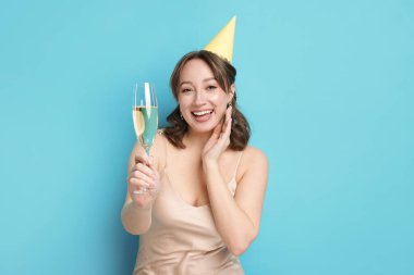 Doğum günü kutlaması. Açık mavi arka planda bir bardak köpüklü şarap içen kadın.