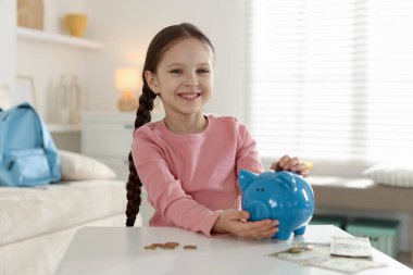 Kız cep harçlığını kapalı bir masadaki domuz kumbarasına yatırıyor.