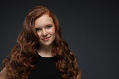 Koyu gri arka planda sağlıklı dalgalı saçları olan güzel bir genç kızın portresi. Metin için boşluk