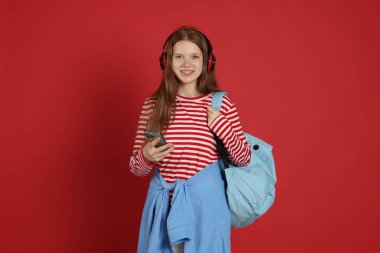 Akıllı telefonlu genç kız kırmızı arka planda müzik dinliyor.