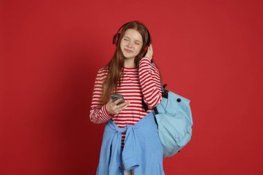 Akıllı telefonlu genç kız kırmızı arka planda müzik dinliyor.