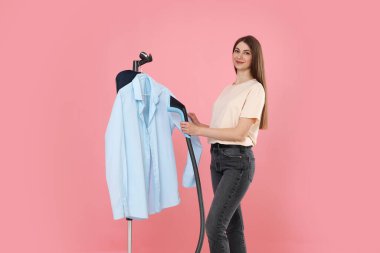 Güzel kadın buharlı gömleği pembe arka planda duruyor.