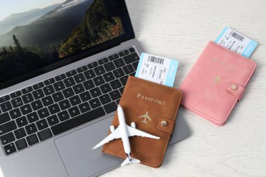 Pasaportlar, uçuş biletleri, uçak modeli ve dizüstü bilgisayar beyaz ahşap masa üzerinde.