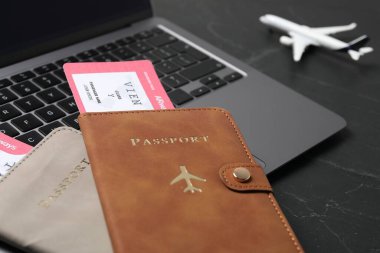 Pasaportlar, uçuş biletleri, uçak modeli ve laptop siyah masada, yakın plan.