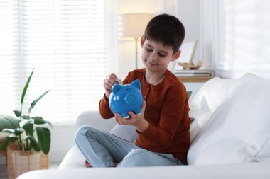 Çocuk cep harçlığını evdeki kanepede domuz kumbarasına yatırıyor.