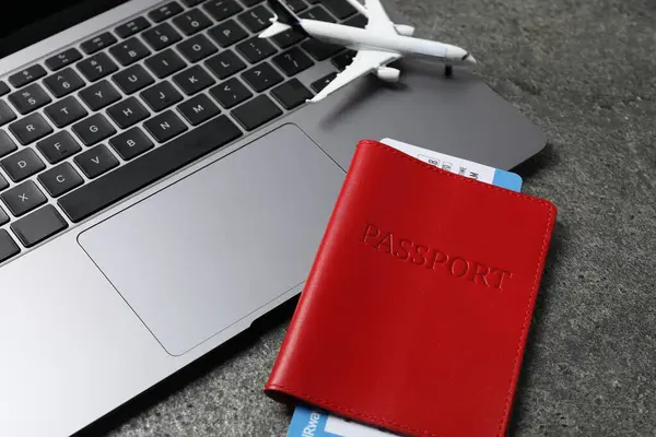 Pasaport, uçuş bileti, uçak modeli ve laptop gri masada, yakın plan.
