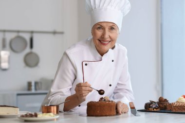Gülümseyen pasta şefi mutfaktaki masada erimiş çikolatayla süsleme yapıyor.