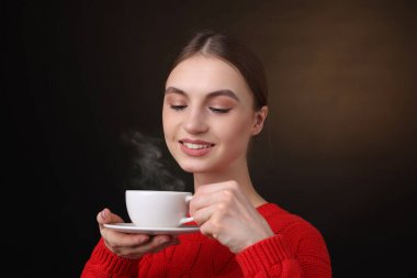 Kahverengi arka planda bir fincan kahveyle gülümseyen kadın.