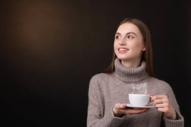 Kahverengi arka planda bir fincan kahveyle gülümseyen kadın. Metin için boşluk