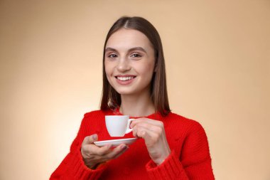 Bej renkli arka planda bir fincan kahveyle gülümseyen kadın