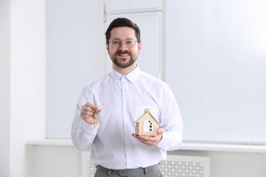 Emlakçının elinde anahtarlık ve ev modeli var.