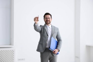 Emlakçının elinde ev şeklindeki anahtarlık ve klasör var.