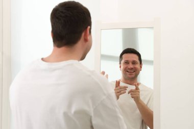 Yakışıklı adam aynada kendine bakıyor.