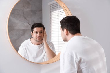 Yakışıklı adam aynada kendine bakıyor.
