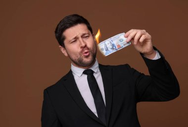 Kahverengi arka planda yanan dolar banknotu olan açgözlü bankacı.