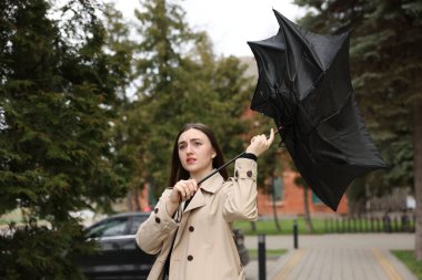 Şemsiyesi kırık bir kadın dışarıda rüzgarla savaşıyor.