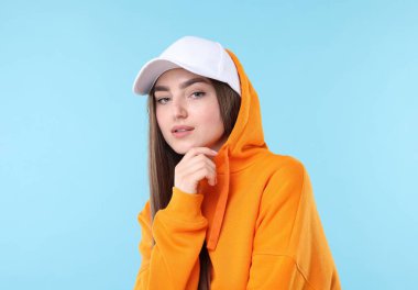 Açık mavi arka planda şık bir beyzbol şapkası takmış güzel bir kadının portresi.