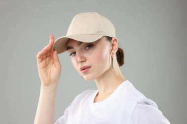 Gri arka planda şık beyzbol şapkalı güzel kadın, yakın plan.