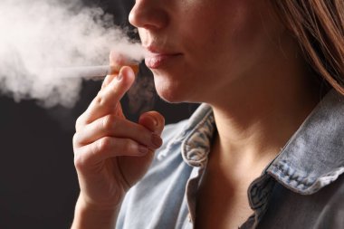 Arka planda sigara içen tişörtlü bir kadın, yakın plan. Kötü alışkanlık.