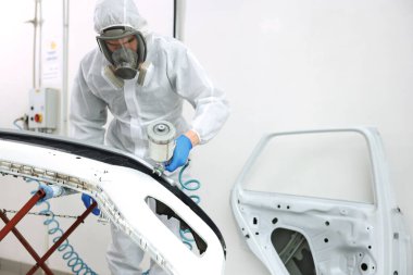 Kaportacıda sprey boyayla araba boyuyor.